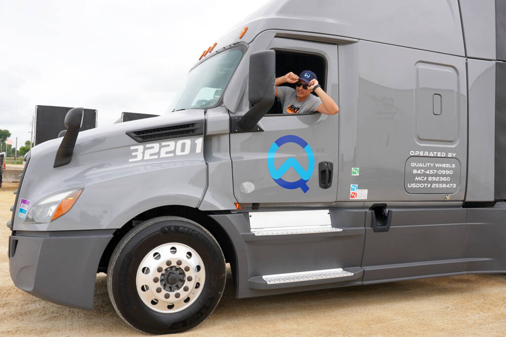 Quality Wheels Inc. CDL-A driver behind the wheel of a Kenworth semi-truck