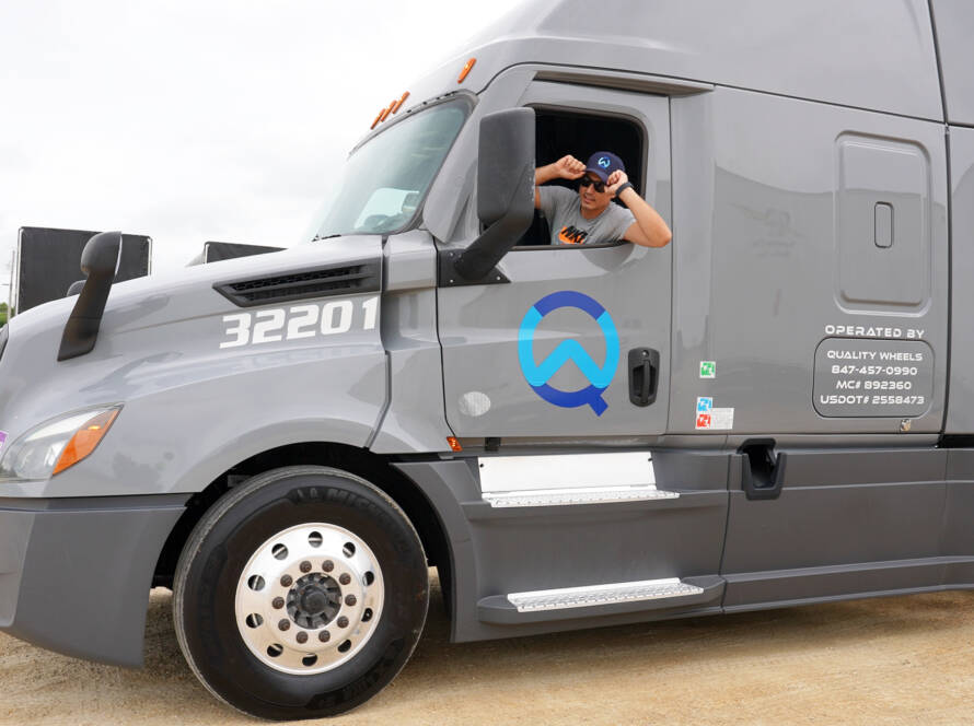Quality Wheels Inc. CDL-A driver behind the wheel of a Kenworth semi-truck