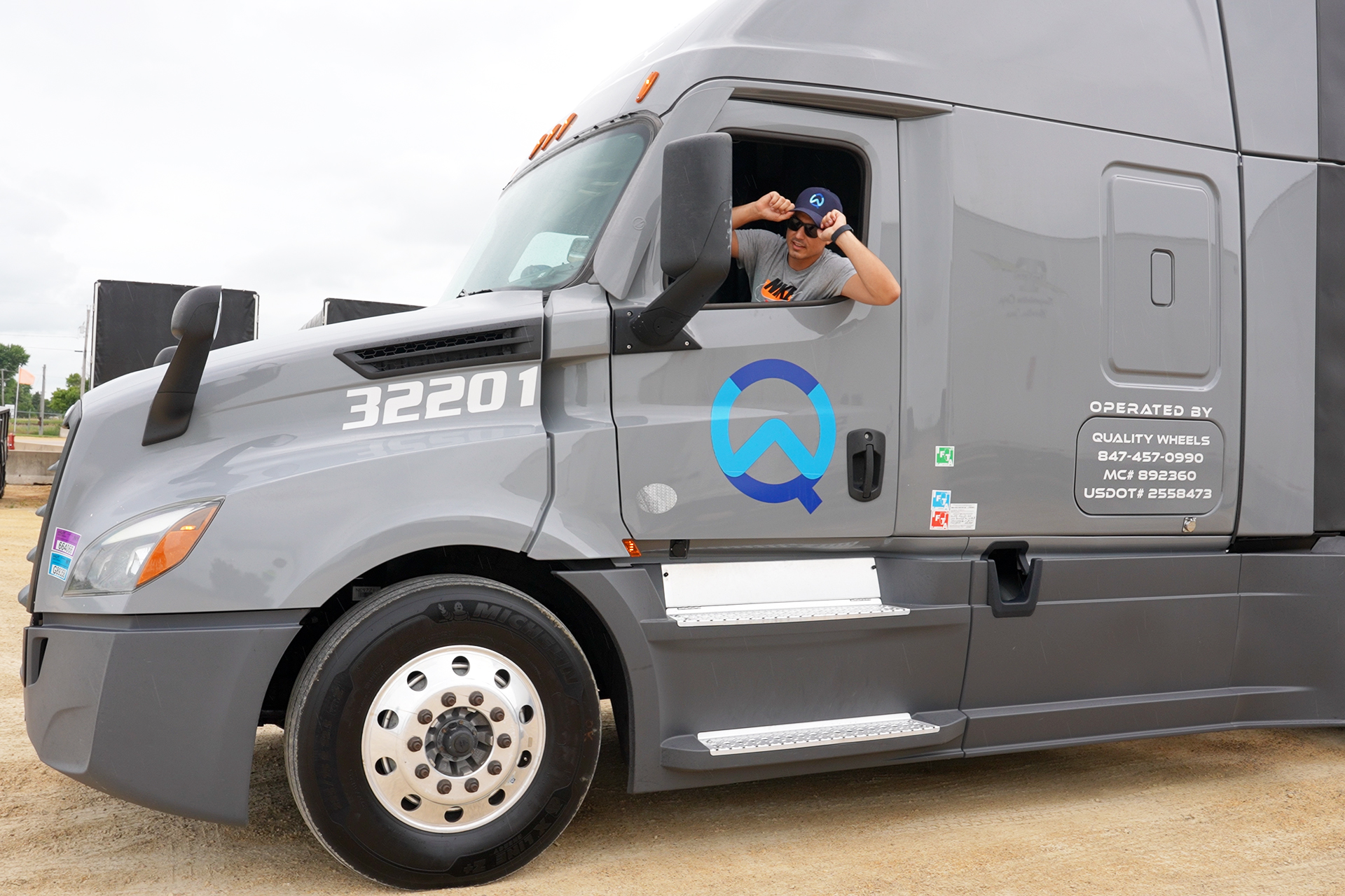 Quality Wheels Inc. CDL-A driver behind the wheel of a Kenworth semi-truck